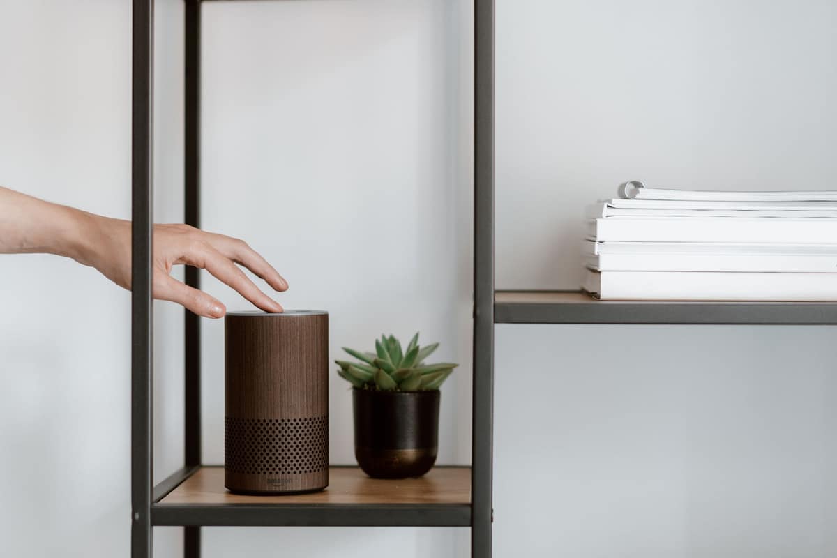 A hand adjusting a smart speaker on a bright shelf