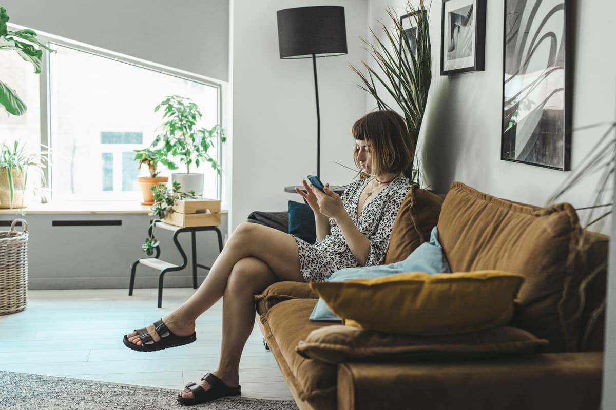 A young woman sitting on a couch looking at her phone in a bright room