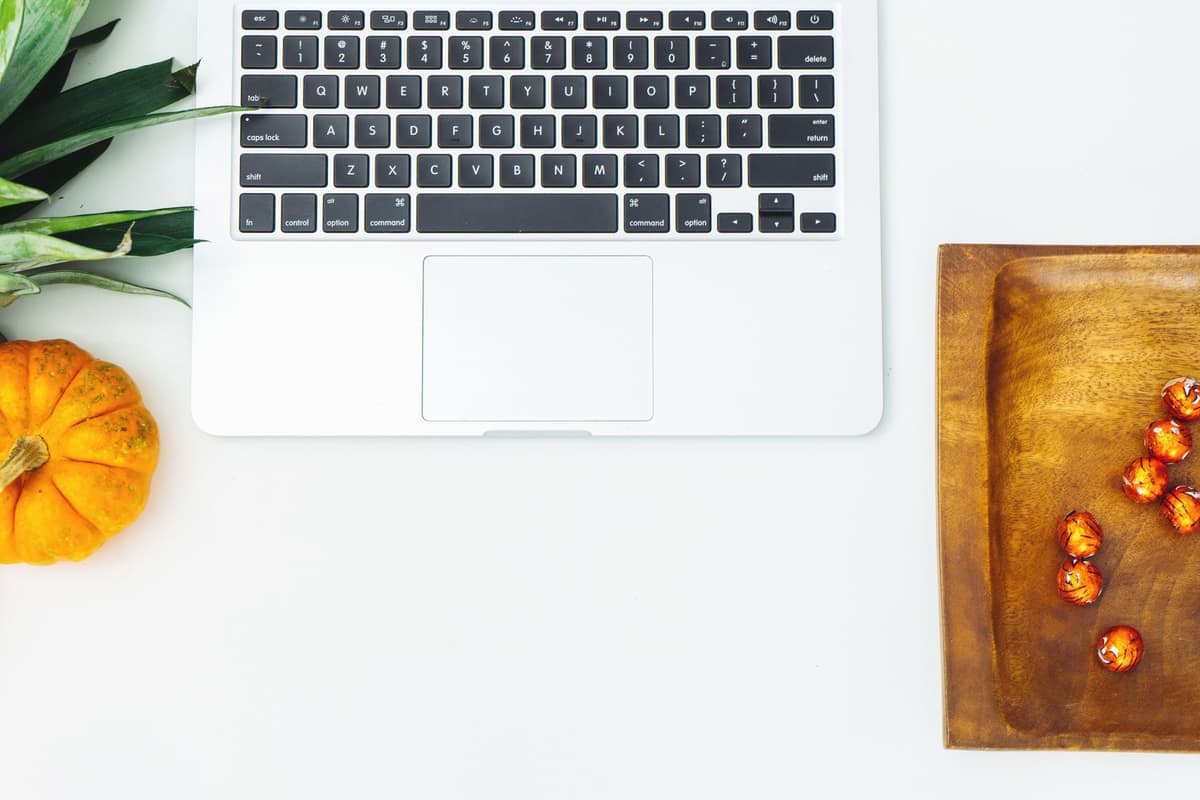 A laptop on a white desk beside a small pumpkin and autumn decorations