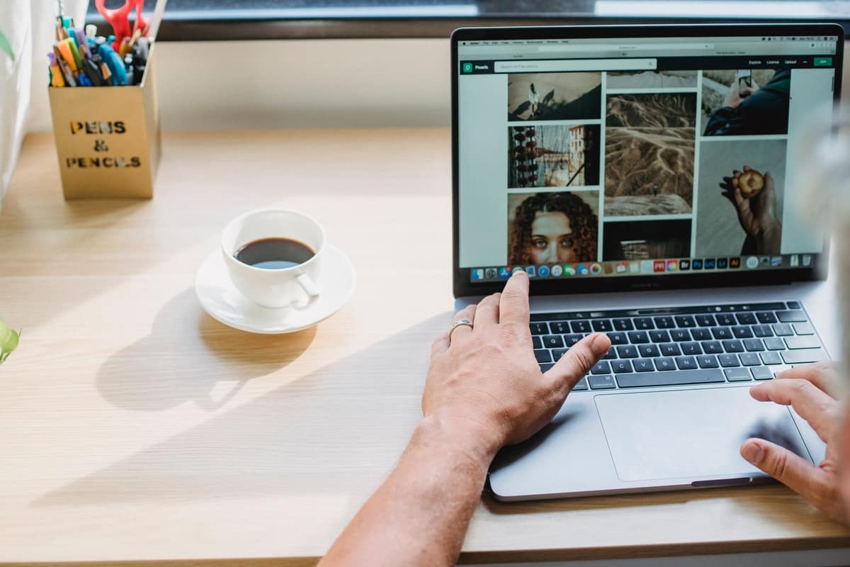 A person browsing on a laptop at a bright desk with a cup of coffee