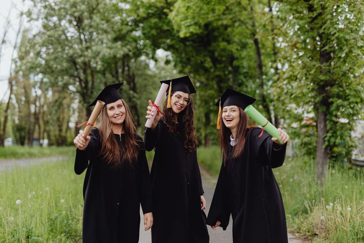 A graduate holding a mortarboard outdoors in sunshine