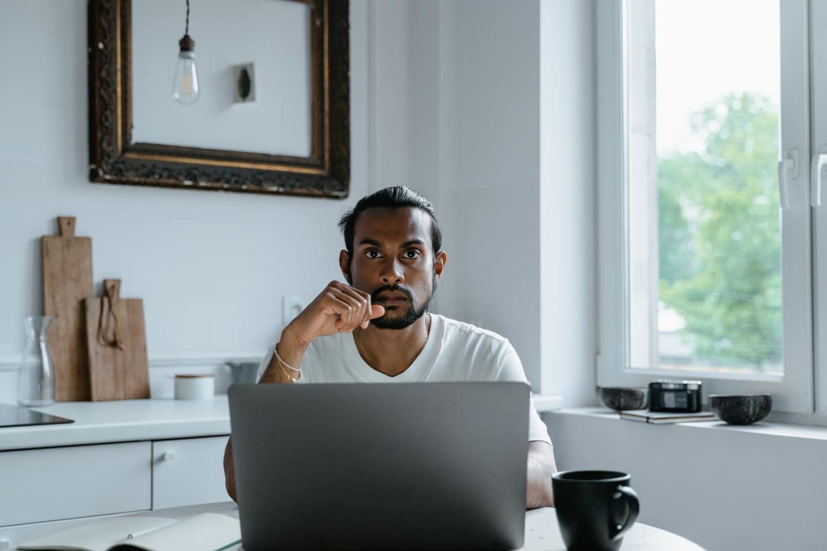 A thoughtful person with a laptop by a bright window