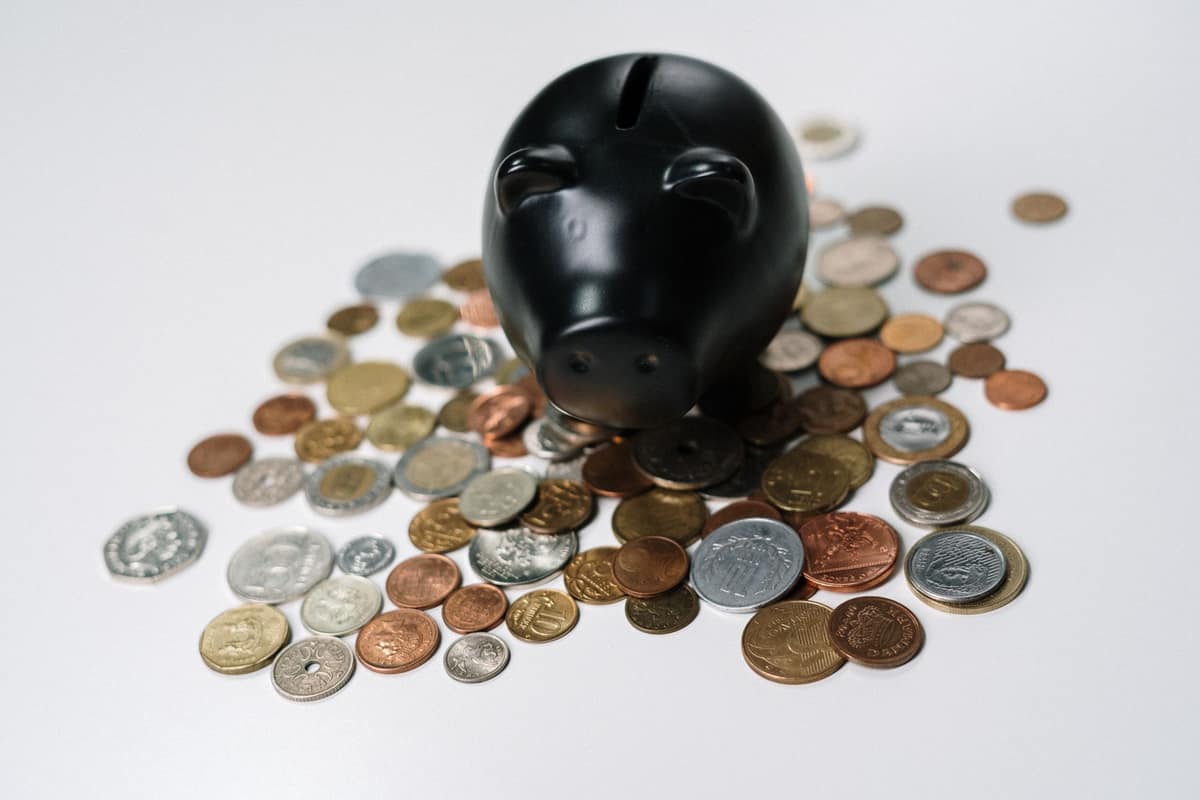 A piggy bank beside a scatter of coins on a white desk