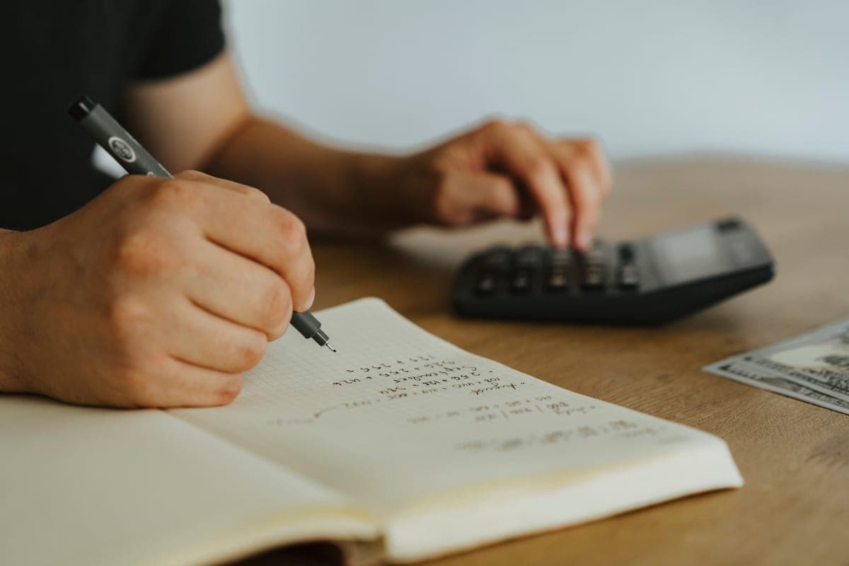 A person working through numbers in a notebook at a bright desk