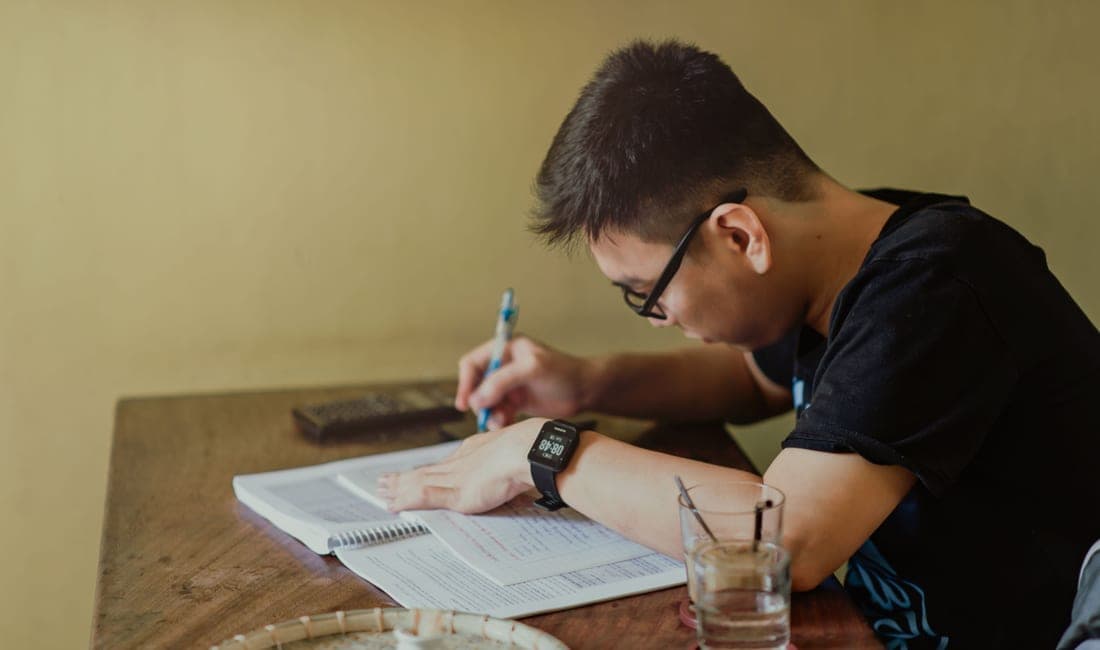 A student reading through notes at a desk beside a bright window