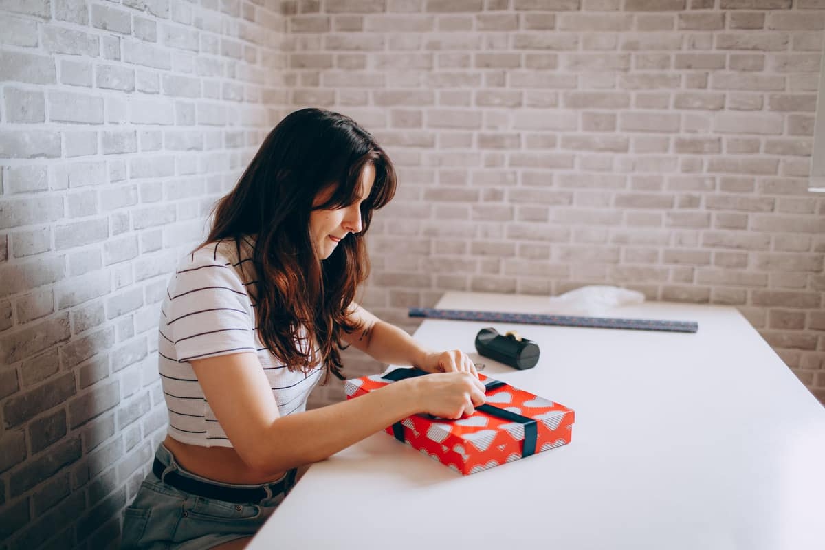 A woman tying a ribbon on a wrapped gift box at a white table