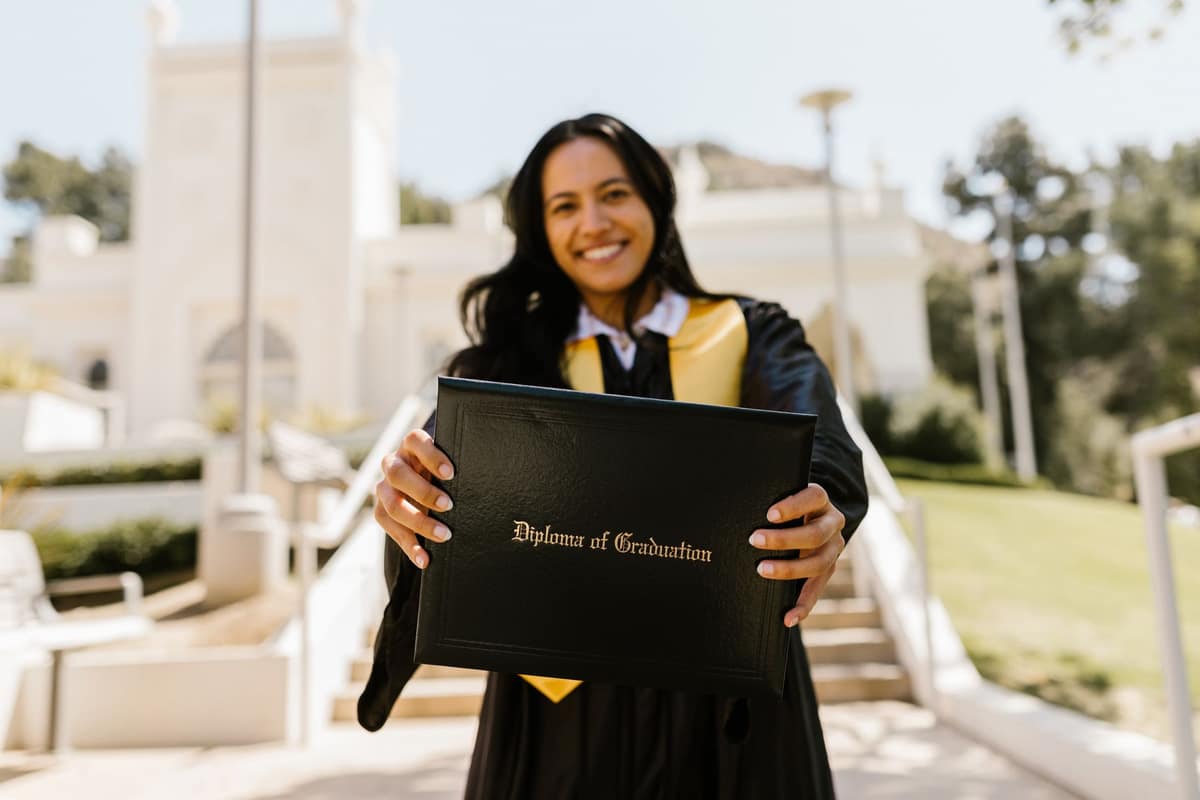 A smiling graduate in a gown holding a diploma outdoors