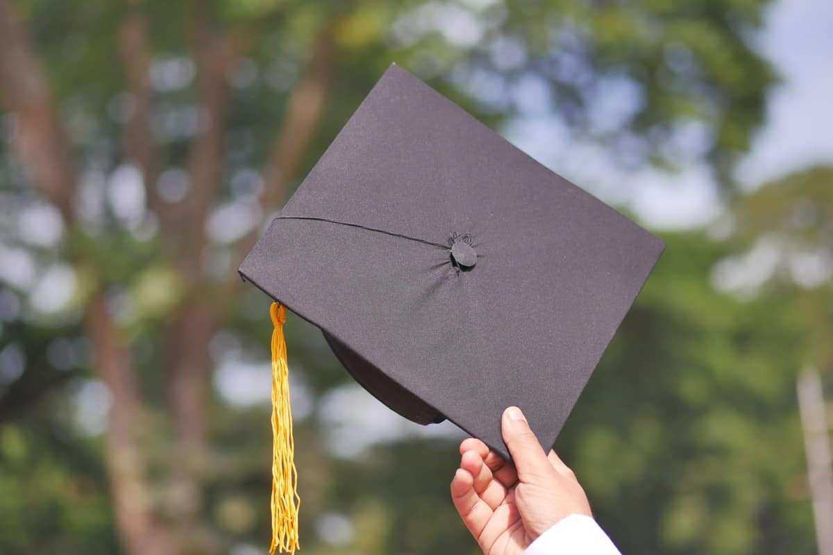 A hand holding a graduation cap against sunlit trees