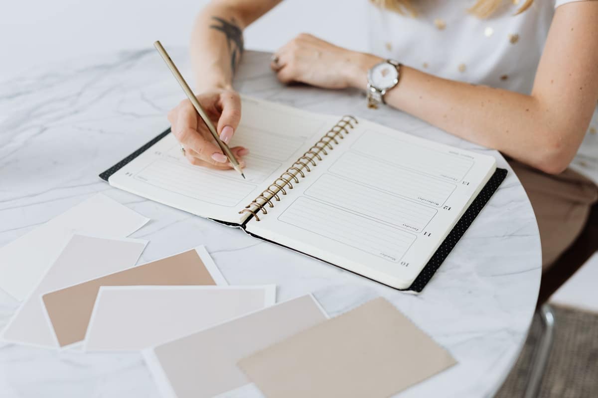 A person writing in a weekly planner at a bright table