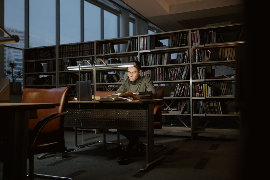 A graduate student working with books and notes in a bright library