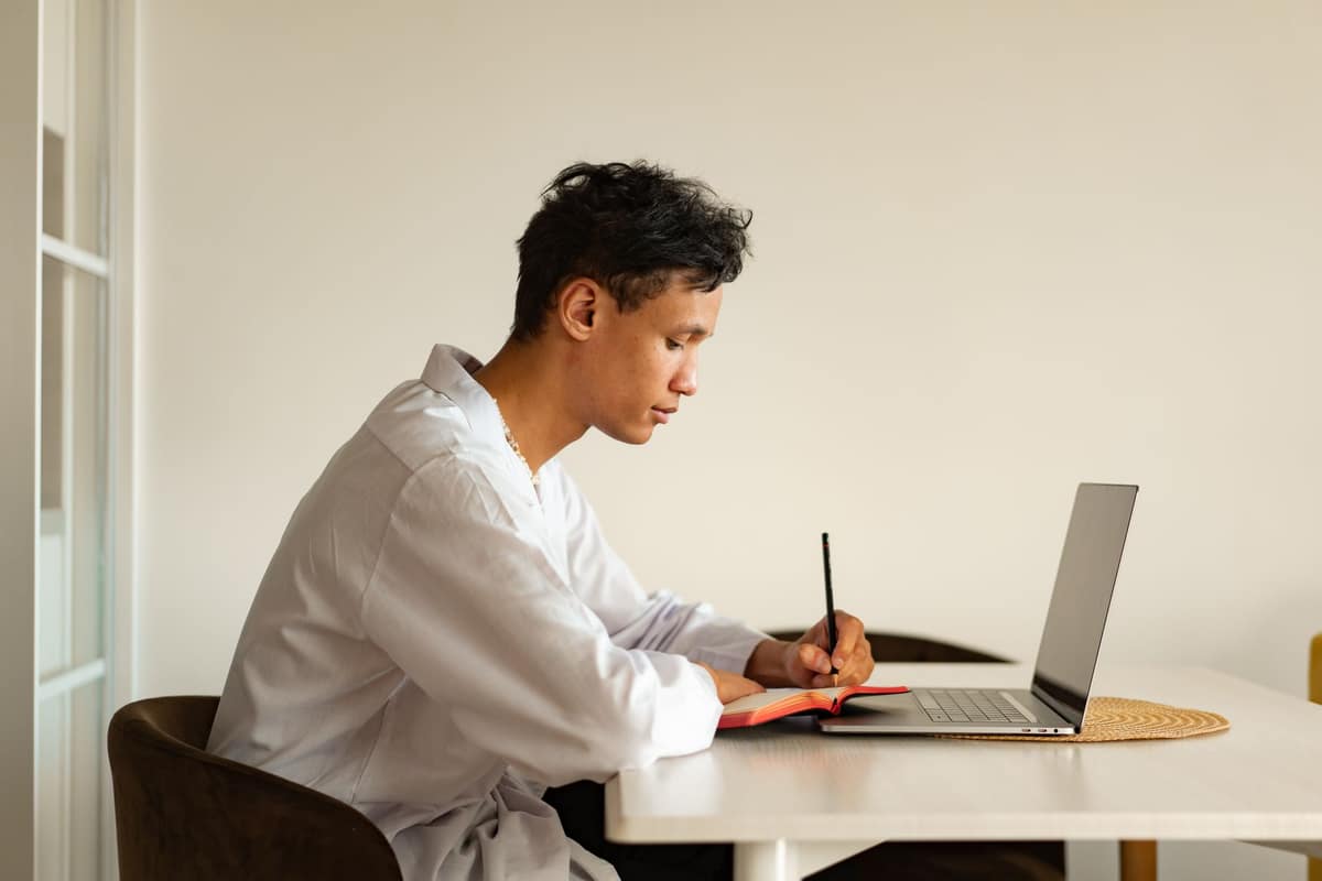 A young man studying at a laptop at a bright white desk