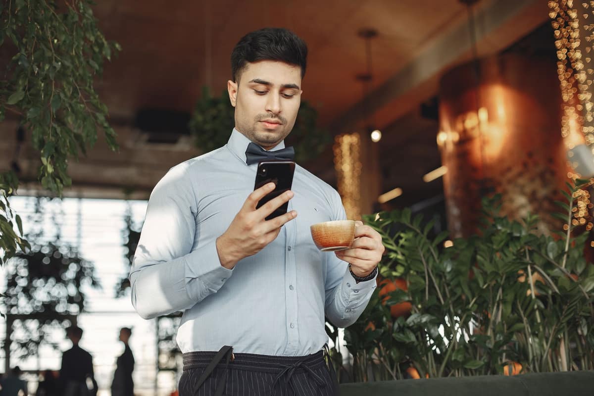 A young man looking at his phone in a bright cafe
