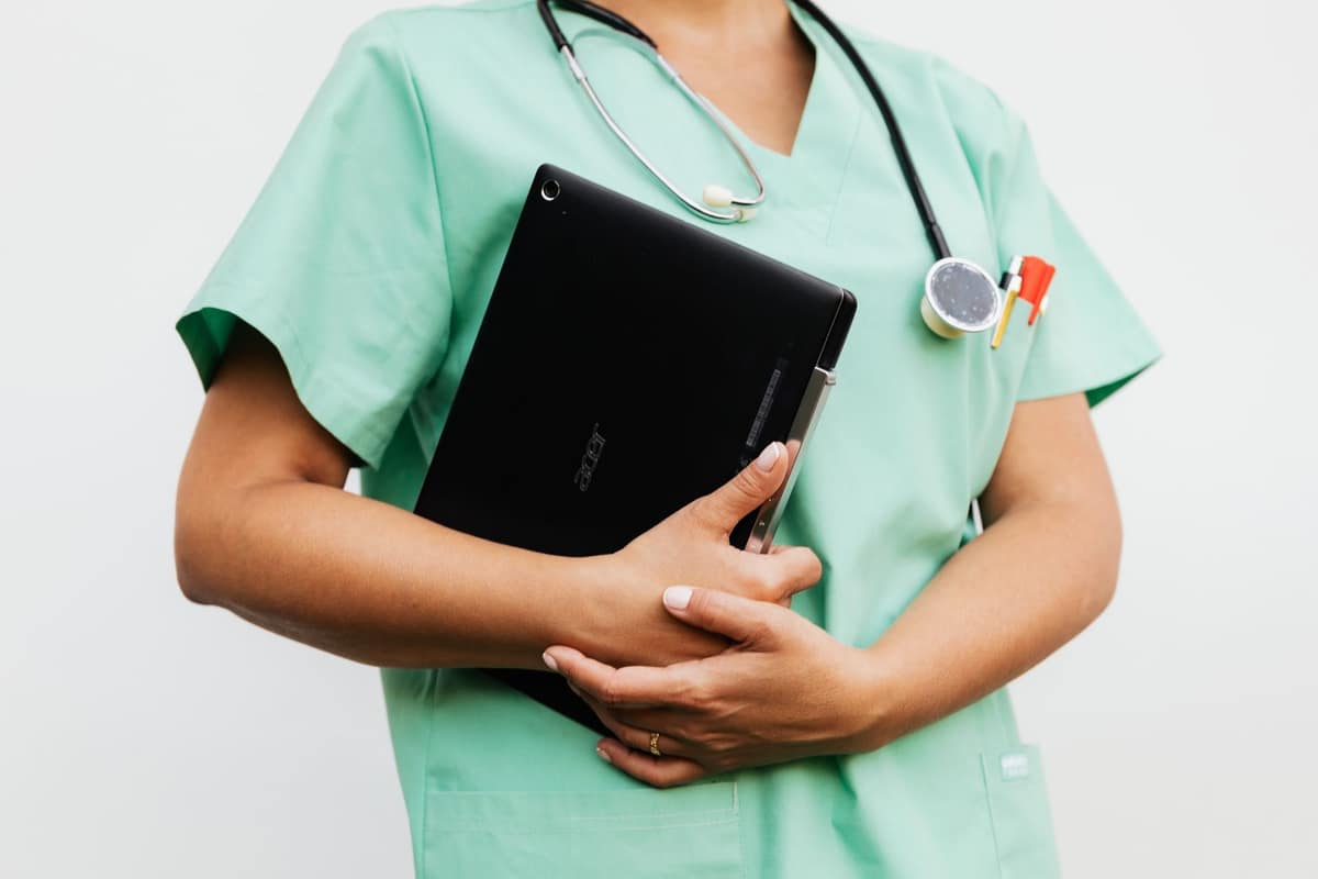 A nursing student in scrubs holding a tablet against a white wall