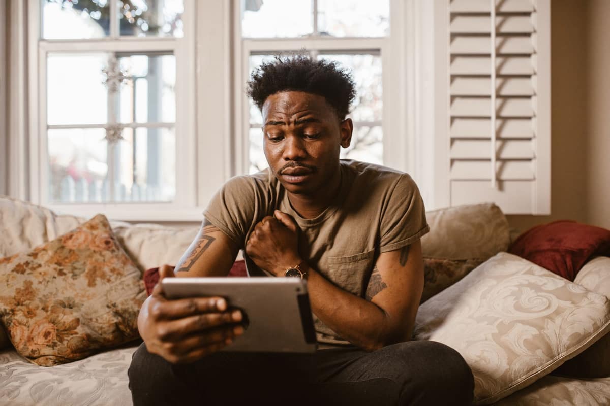 A young man on a sofa looking at a tablet in a bright living room