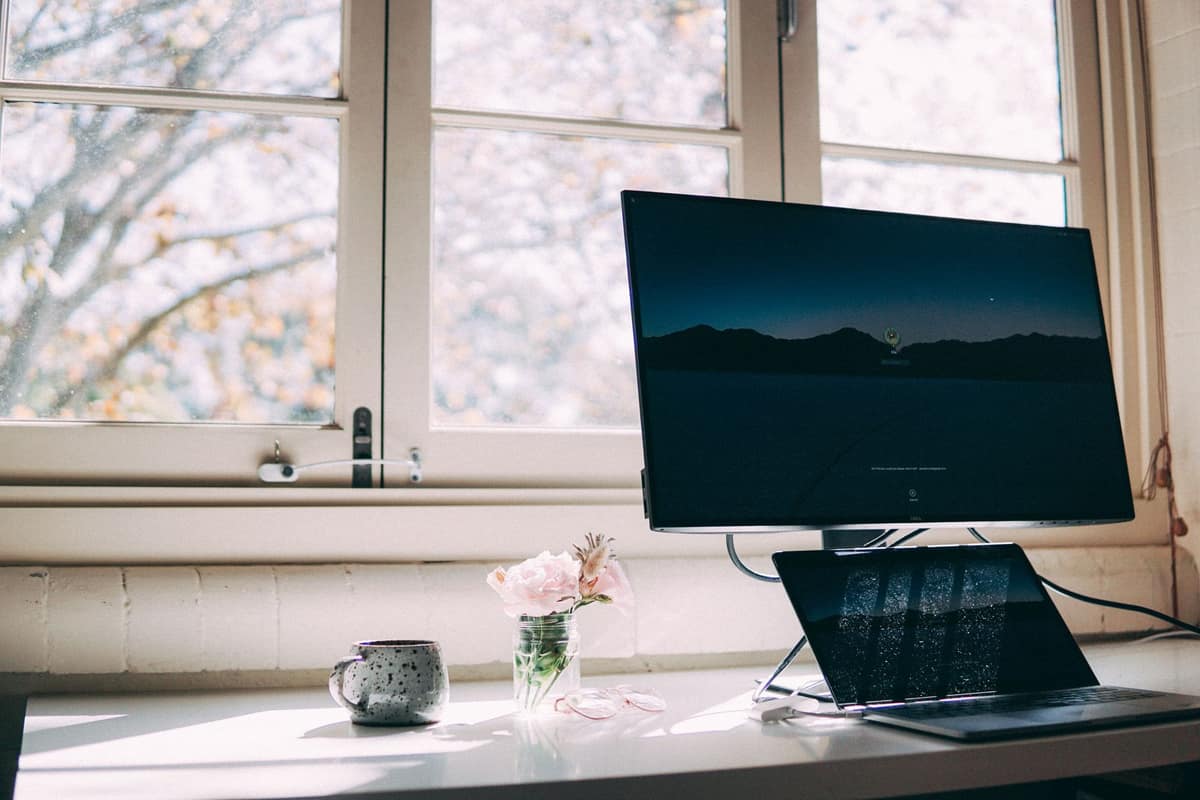 A person opening a laptop at a bright desk in the morning