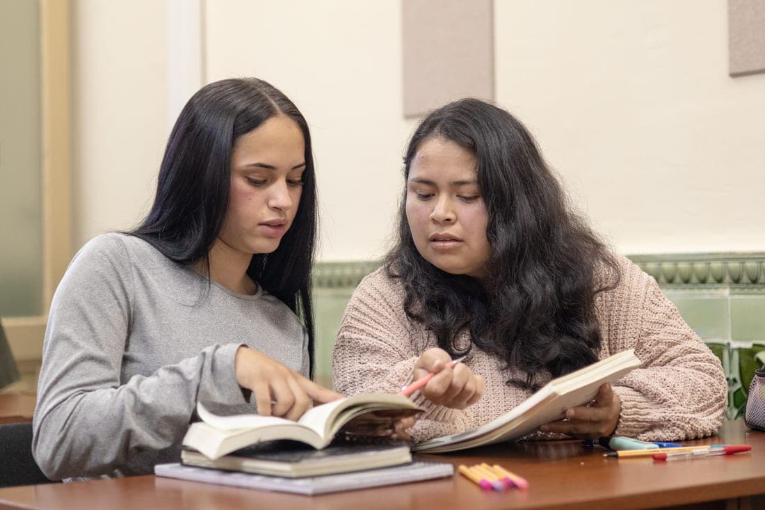 Two students working together at a table in a bright library
