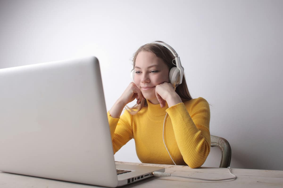 A student in headphones smiling at a laptop in a bright room