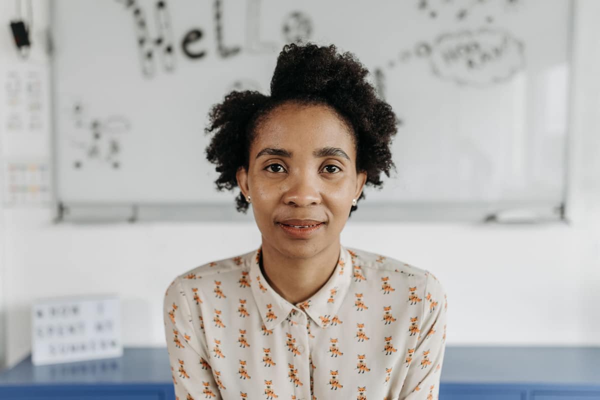A smiling teacher standing in front of a whiteboard in a bright classroom